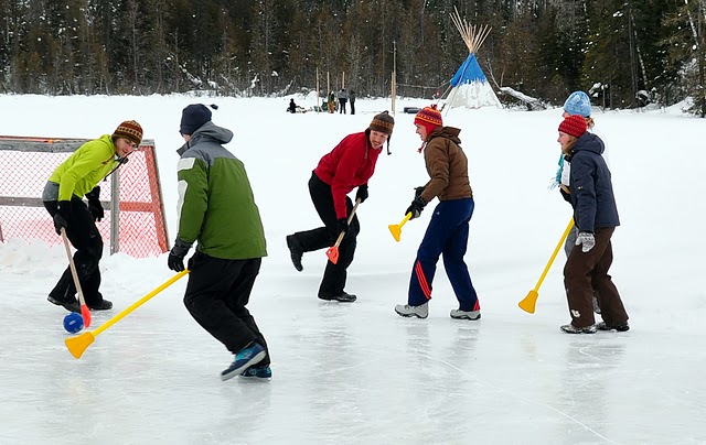 A group of people play broomball on a lake with a teepee in the background