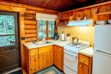 Kitchen inside log cabin with gas stove, white fridge, and door leading to deck