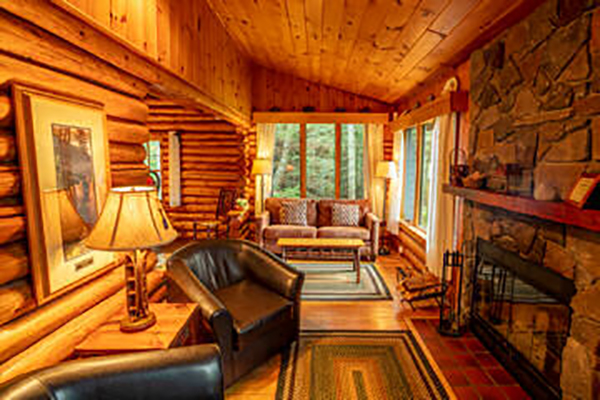 Living area of log cabin with stone fireplace and two brown chairs