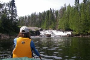 Shot from behind of woman in yellow life jacket canoeing towards waterfall