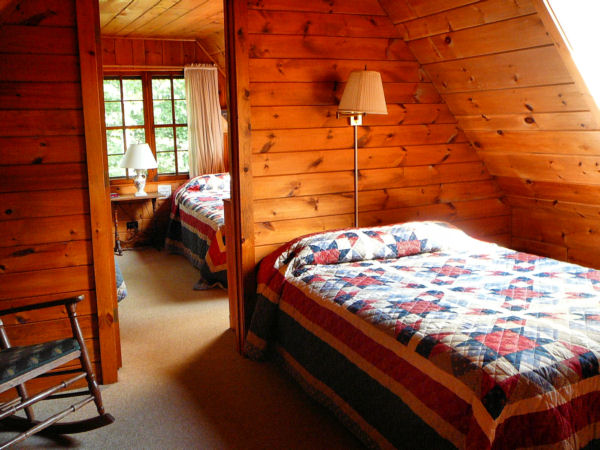 Bedroom in log cabin with quilted bedspread and open door to second bedroom