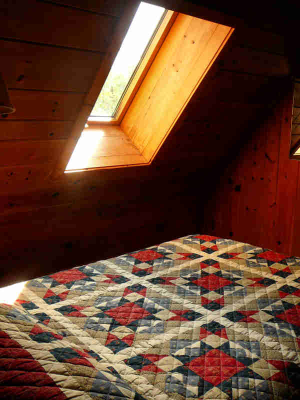 Bed in a log cabin with quilted bedspread and skylight