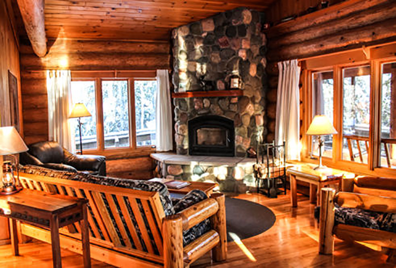 Living area of a log cabin with stone fireplace and wooden couches