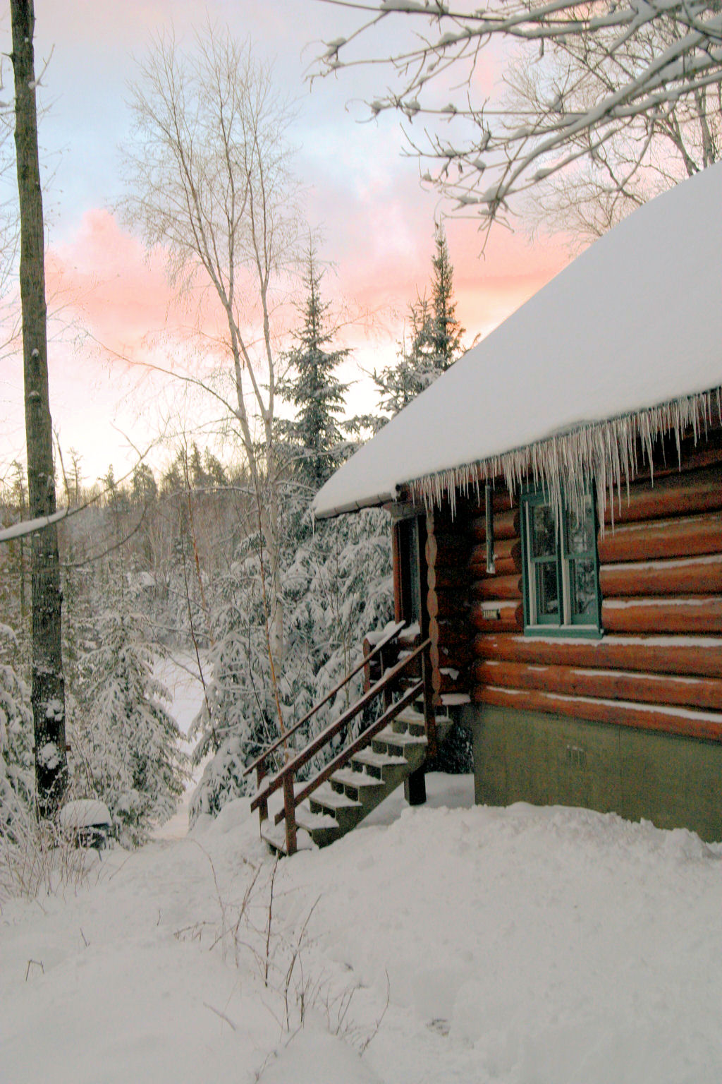 Outside of log cabin with icicles hanging from roof and stairs leading to front door in winter