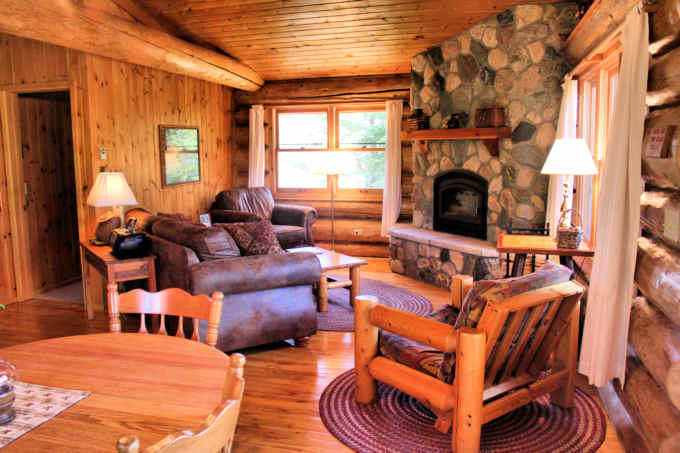 Living area of a log cabin showing brown couch and chair and stone fireplace