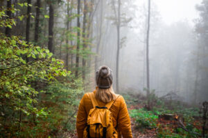 Woman with knit hat and yellow backpack hiking in foggy woodland