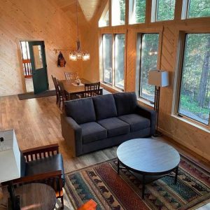 Living area of log cabin with large windows, brown couches and a bear patterned rug