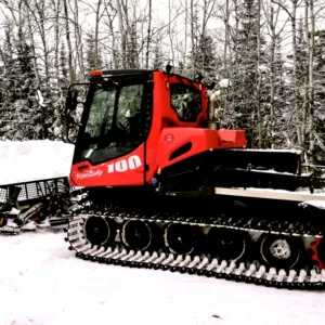 Red and black ski trail grooming tractor in the snow in the woods.